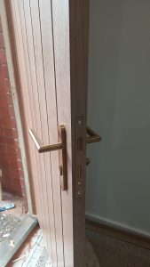 Close-up of a wooden door with a brass lever handle and lock mechanism; door is slightly ajar.