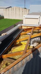Rooftop renovation: exposed wooden rafters, yellow insulation, and a silver HVAC duct running through the space.